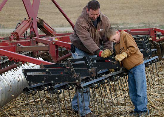 Son helping father with farming equipment.