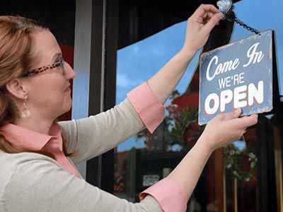 Woman hangin a we're open sign.